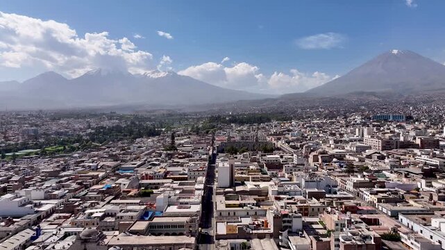 Aerial drone view of Arequipa, Peru, showcasing the urban landscape with the iconic Misti volcano rising in the background under a clear blue sky. Scenic cityscape in southern Peru.