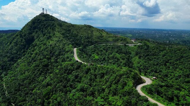 Static aerial frame capturing the elevated landscape surrounding People's Park in the Sky with lush greenery, forested hills, and the winding Tagaytay&ndash;Calamba Road during bright daylight.