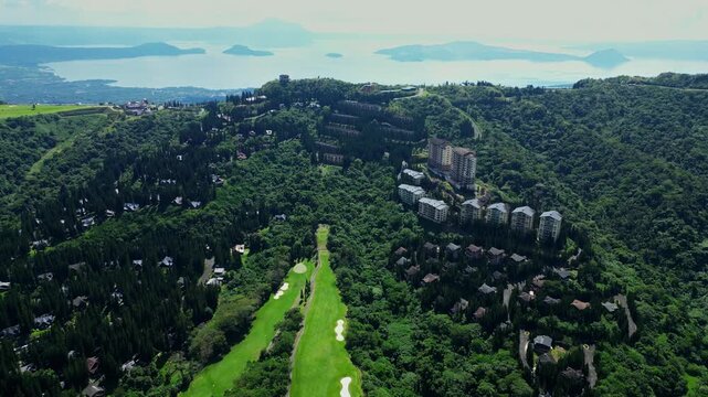 Wide establishing aerial shot of Woodridge Place at Tagaytay Highlands in Cavite Philippines showcasing luxury accommodations,Taal Volcano view golf course and rolling mountain landscapes at noon time