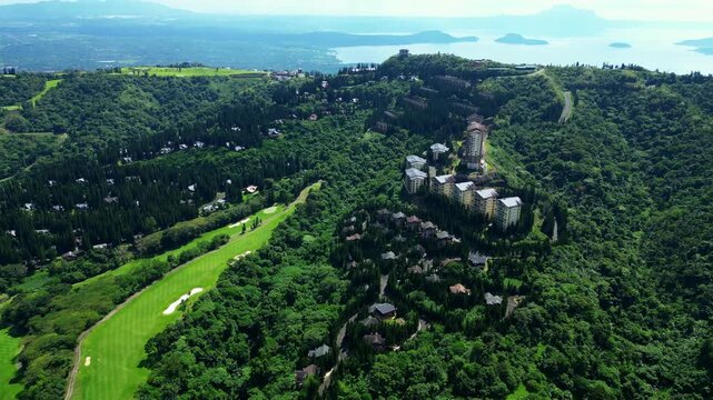 Wide angle aerial shot highlighting luxury resort Tagaytay Highlands developments, tropical forests, winding mountain roads, and panoramic views across Taal Lake toward Taal Volcano.