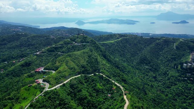 Wide cinematic landscape featuring the scenic People's Park in the Sky road, lush mountain forests, within Tagaytay Highlands overlooking Taal Volcano and the expansive waters of Taal Lake.