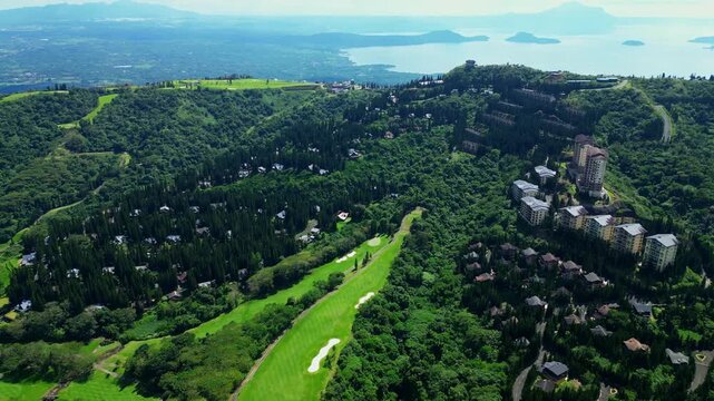 Wide angle drone shot featuring the beautifully developed Woodridge Place, lush forests, scenic mountain road, and breathtaking views of Taal Volcano and Taal Lake in Tagaytay City Cavite Philippines.