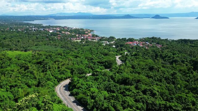 Wide cinematic panorama featuring a Talisay residential are in batangas surrounded by dense greenery and natural forest landscapes Taal Lake as background during daytime.