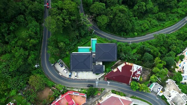 Slow pulldown drone footage flying above a luxury private residence along Ligaya Drive in Talisay Batangas Philippines featuring modern architectural design, an elongated swimming pool, and greens.