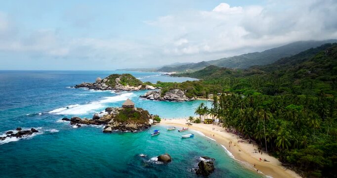 Drone view of thatched palapa on small rocky peninsula surrounded by turquoise ocean waters at Cabo San Juan de Guia in Tayrona National Park, Colombia