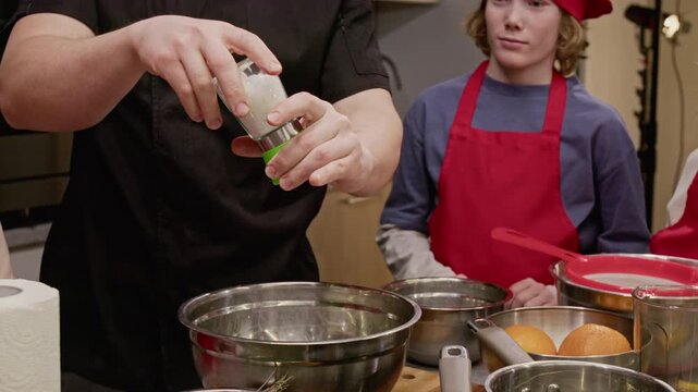 Unrecognizable male chef seasoning food with grinder during culinary class for teenagers. Perfect for promoting cooking schools, kitchenware brands, educational workshops