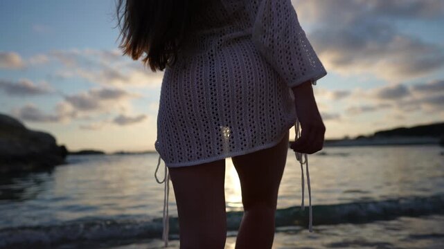 Woman wearing a pareo walking on the beach at sunset