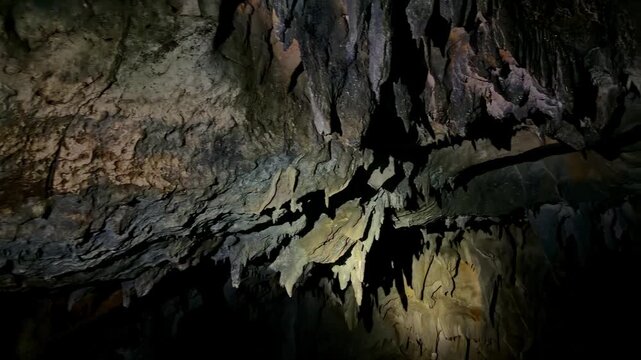 Flashlights reveal rocky textures inside a deep, dark cave environment.