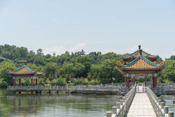 Fototapeta premium Scenic view of a traditional Chinese pavilion and bridge corridor across a peaceful lake under blue sky