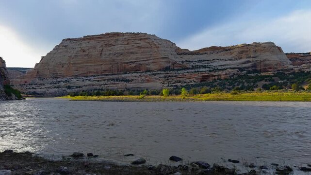 Harding Hole backcountry camping overlook spot, Yampa River beneath rugged canyon slopes and layered rock formations under cloudy skies, establishing pan right