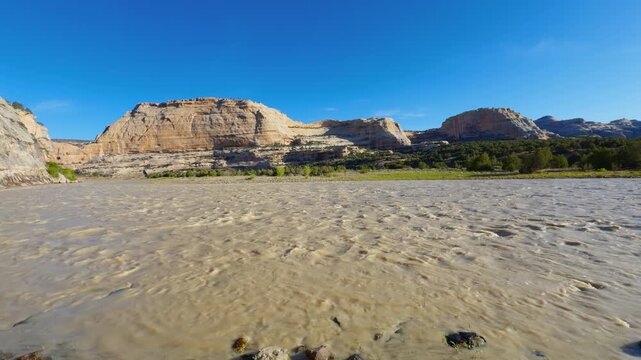 Harding Hole backcountry camping overlook spot, sandy riverbank and desert canyon terrain beneath clear blue skies in Colorado, muddy water rippled texture in the morning