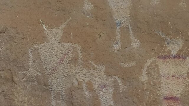 Ancient pictograph figures painted on weathered sandstone surface, hands and pointed horn heads
