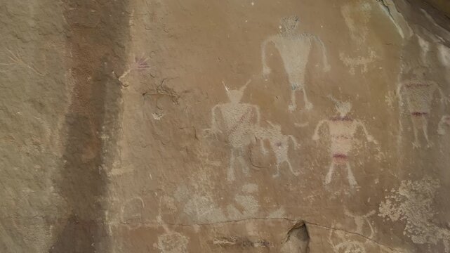 Faded human figure pictographs preserved on sandstone wall at archaeological site, subtle shaded differences and story of native culture