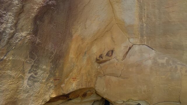 Ancient pictographs painted on sandstone cliff wall in arid canyon landscape, faded light pigments on stone