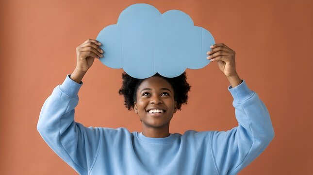 Happy young woman holding a light blue cardboard cloud shape above her head against a solid warm brown studio background
