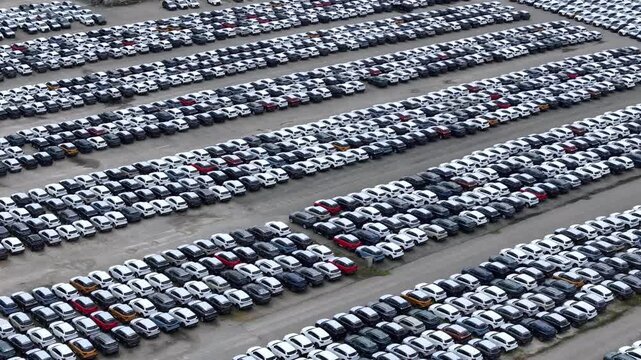 Finished crossover SUVs fill dense parallel storage rows inside a major automotive logistics compound awaiting shipment, wholesale distribution and dealer allocation, aerial slide.
