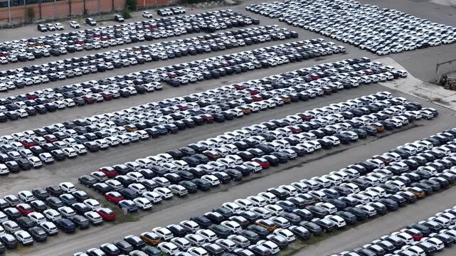 Finished crossover SUVs occupy dense parallel storage rows across a large automotive logistics compound awaiting shipment, dealer allocation and wholesale distribution, aerial slide.