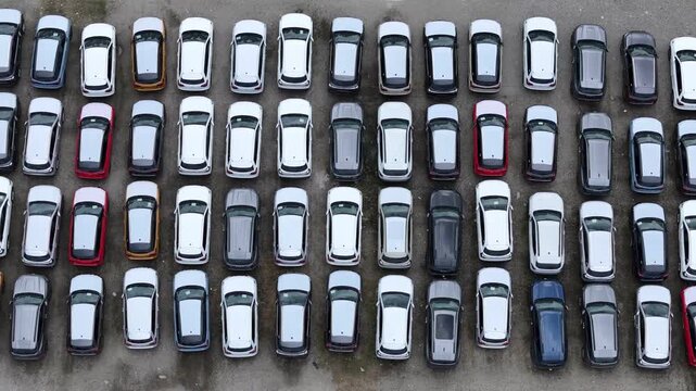 Finished crossover SUVs form dense geometric storage rows across a major automotive logistics compound awaiting shipment, dealer allocation and wholesale distribution, drone pullback with parallax.