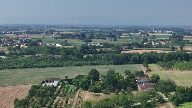 Po Valley farmland stretches across Northern Italy with cultivated fields, farmhouses, tree lined shelterbelts and scattered rural settlements, illustrating intensive agriculture, drone flyover.