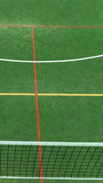 Dynamic aerial shot of a vibrant green multisport court, featuring a basketball hoop shadow and a tennisvolleyball net. Perfect for sports, fitness, and active lifestyle projects.