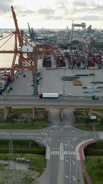 Cinematic aerial shot of a busy maritime terminal in Gdynia, Poland, featuring cargo ships, cranes, and a truck crossing the estakada bridge during golden hour.