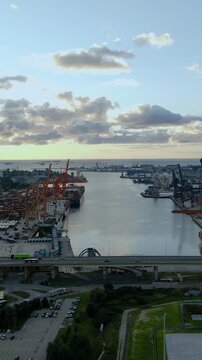 Cinematic aerial shot of the industrial port in Gdynia, Poland, featuring cargo ships, cranes, and the Estakada Kwiatkowskiego bridge during golden hour.