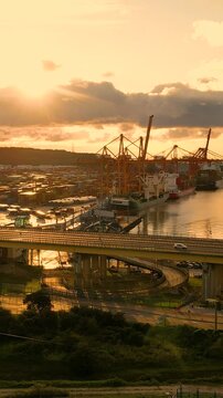 A cinematic sunset over the industrial port of Gdynia, Poland, featuring cargo ships, cranes, and traffic on the Estakada bridge. Suitable for logistics and global trade concepts.