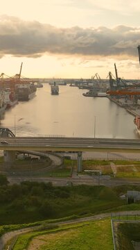 An aerial cinematic view of the Gdynia mobile port in Poland during a golden sunset, featuring cargo ships, cranes, and traffic on the Estakada bridge. Ideal for logistics and global trade concepts.