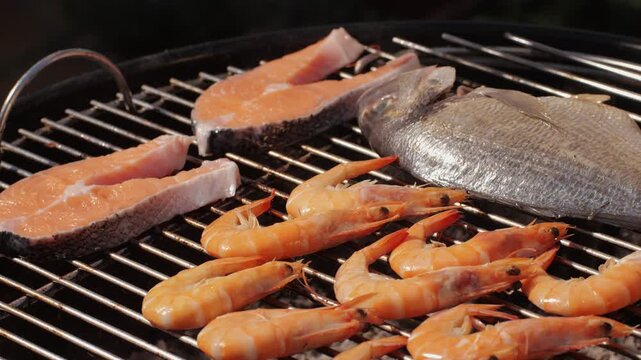Chef cooking shrimps with oil and spices on grill close-up. Prawns on fire throwing them on pan. Dorado and salmon fish steak on frying grill. Restaurant Food concept. Sea