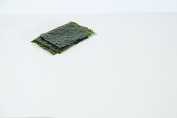 Several sheets of dark green seaweed rests on white background. Texture appears slightly rough and naturally frayed at edges. Minimalist composition emphasizes products natural appearance © Nurma