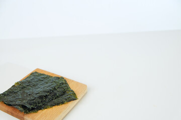 Fresh seaweed sheets rest on a light wooden board. Simple, clean background highlights natural texture and color. Ideal for health, wellness, or Asian cuisine content © Nurma