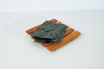 Dark seaweed rests on wooden sticks. Simple background highlights natural textures. Ideal for health, wellness, or Asian food themes. Clean composition evokes calm and purity © Nurma