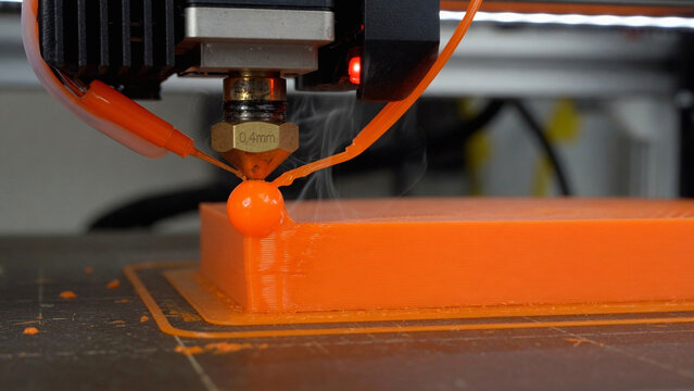 A 3D printer creates an orange object on a dark surface with precision technology.