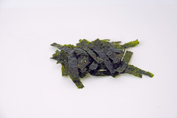 Dark green seaweed pieces lie scattered. They rest on a plain white background. The texture appears dry and brittle. Natural, organic shape with irregular edges. Suitable for food, health © Nurma