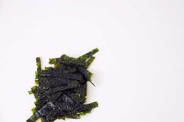Dark green seaweed pieces lie scattered. They rest on a plain white background. The texture appears dry and brittle. Natural, organic shape with irregular edges. Suitable for food, health © Nurma