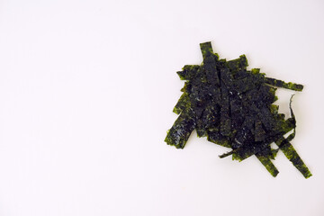 Dark green seaweed pieces lie scattered. They rest on a plain white background. The texture appears dry and brittle. Natural, organic shape with irregular edges. Suitable for food, health © Nurma