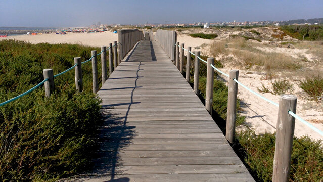 POV perspective of a wooden boardwalk path through the sand dunes of Paramos beach in Portugal