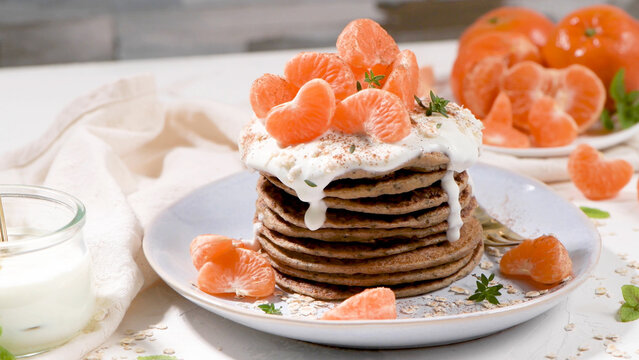 Stack of homemade oatmeal pancakes topped with fresh mandarin segments and creamy yogurt