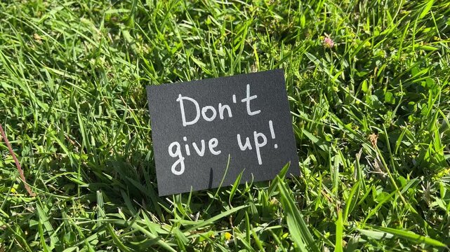 Don&rsquo;t give up - black note with encouragement and support text on the grass in the background