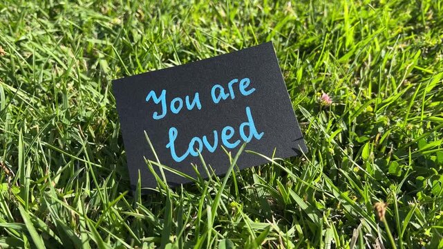 You are loved - black note with encouragement and support text on the grass in the background