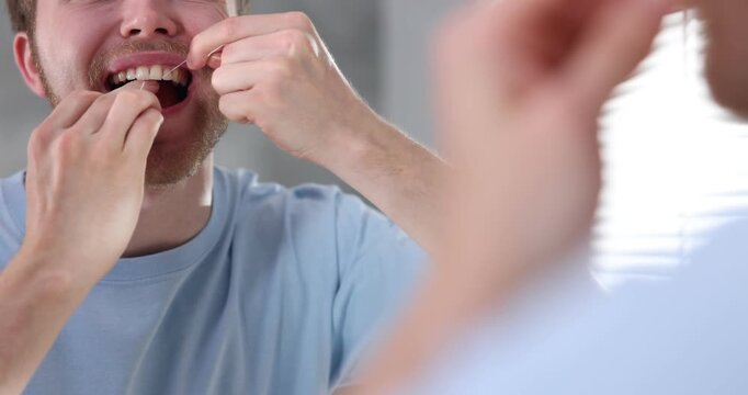 Man using dental floss near mirror indoors, closeup. Oral hygiene