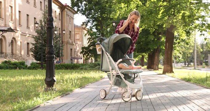 Baby carriage. Mother talking on smartphone while walking with her child in stroller outdoors