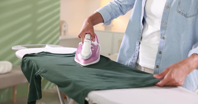Woman ironing long sleeve shirt on board at home, closeup. Camera moving