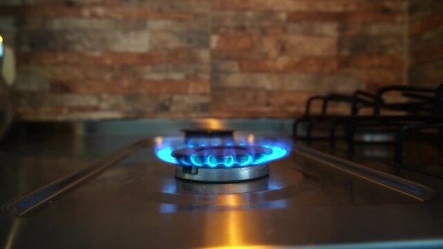 Close-up of a gas stove burner igniting with a bright blue flame on a stainless steel cooktop