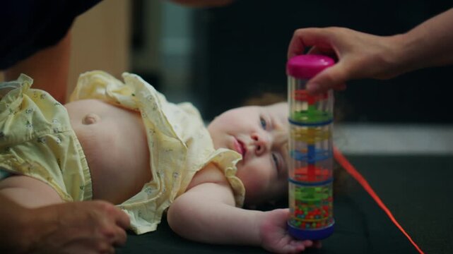 Baby lying on a soft mat while reaching for a colorful sensory toy, with an adult nearby supporting play and early childhood learning