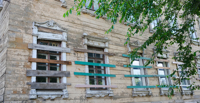 The facade has windows, an old abandoned and ruined wooden house. The windows are boarded up.