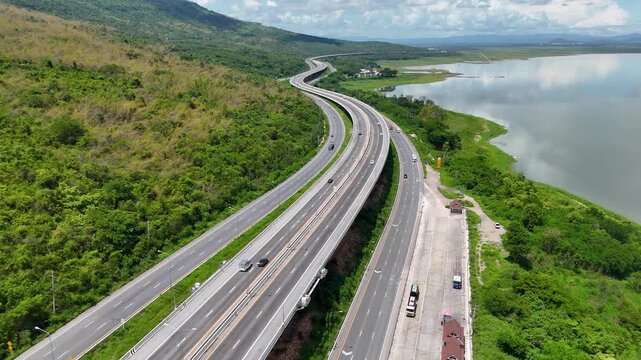 Aerial view of highway running along river and green hills. Transportation, infrastructure, travel and logistics concept