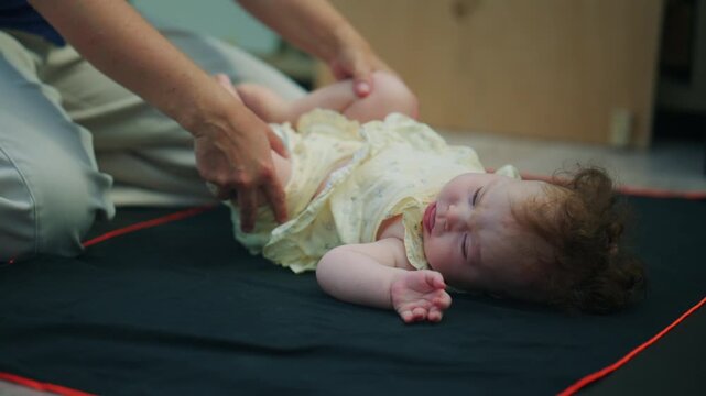 Baby being gently supported by a caregiver during mobility exercises on a soft indoor mat, creating a tender caregiving and early development scene
