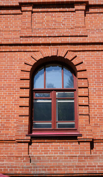 Elegant stone arched window with a wooden frame. Red stone wall, sunny day.