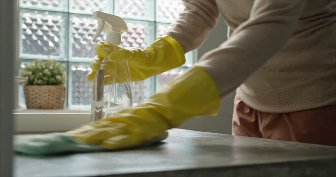 Close up. Asian Woman Hand Spraying Detergent and Wiping Bathroom Sink with Microfiber Cloth, Wear yellow rubber gloves, Housekeeping Hygiene Routine.